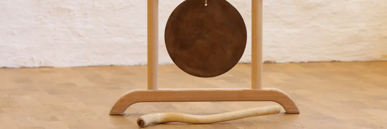 Großer Gong hängt an Holzgestell am Boden.