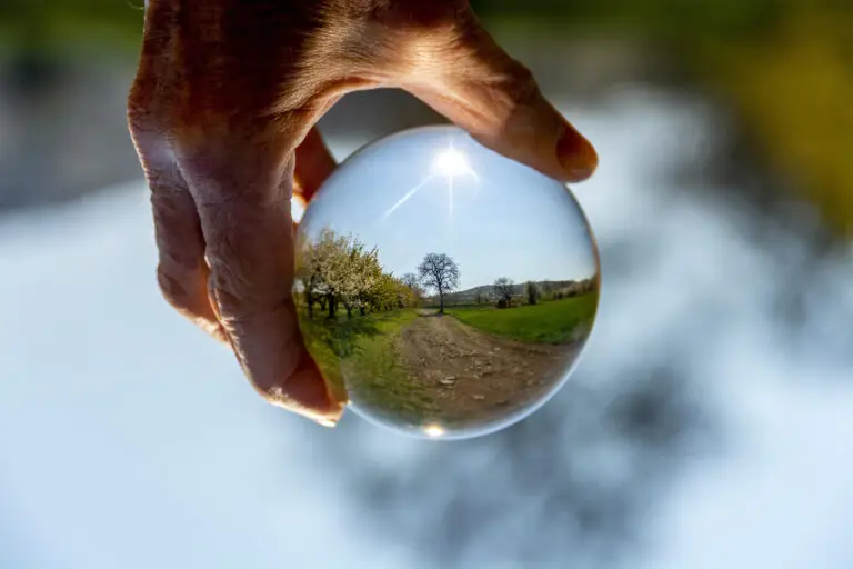 Hand hält Glaskugel mit gespiegelter Landschaft.