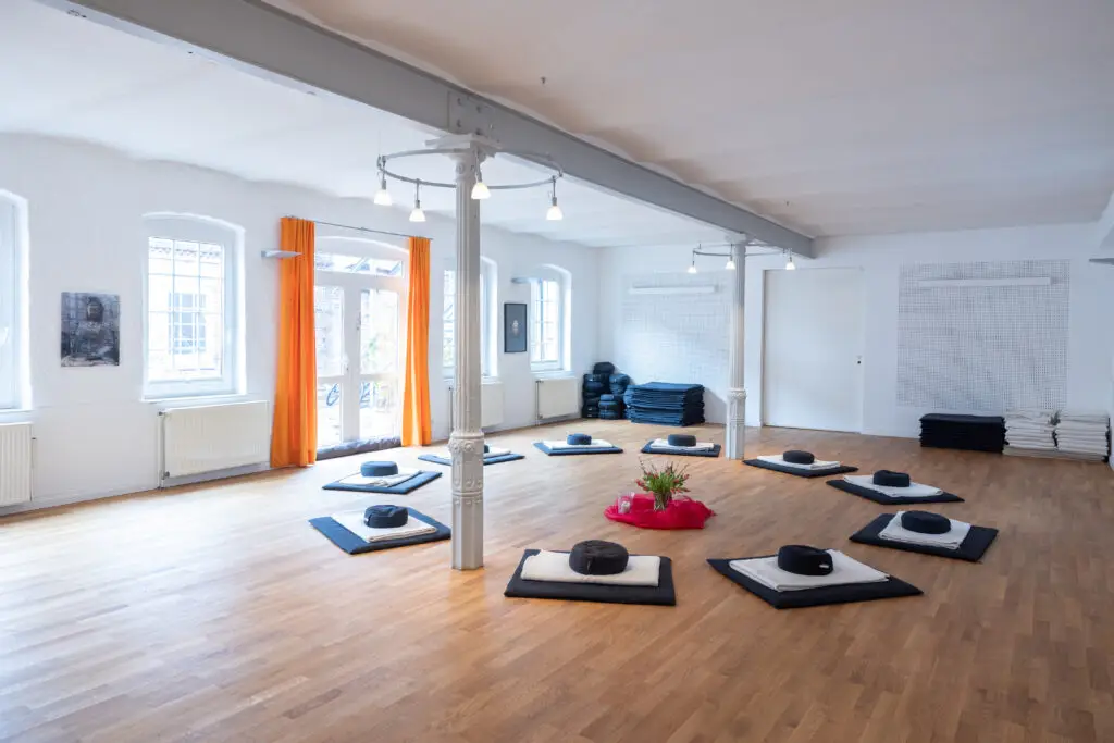 Heller Meditationsraum mit kreisförmig angeordneten Sitzkissen.