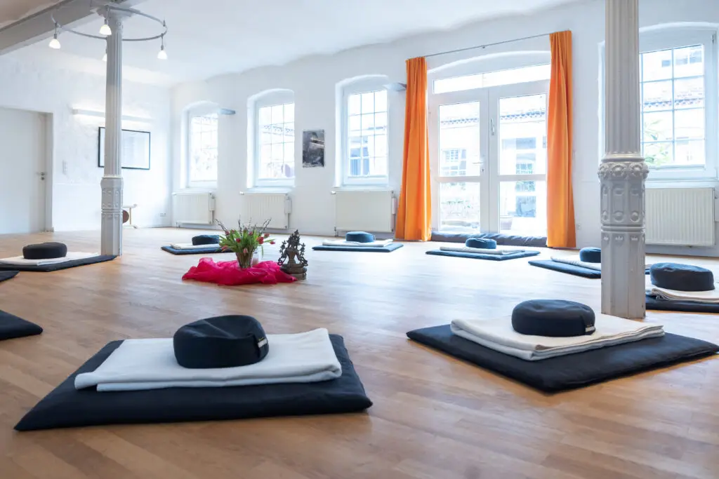 Heller Meditationsraum mit Säulen und Sitzkissen.