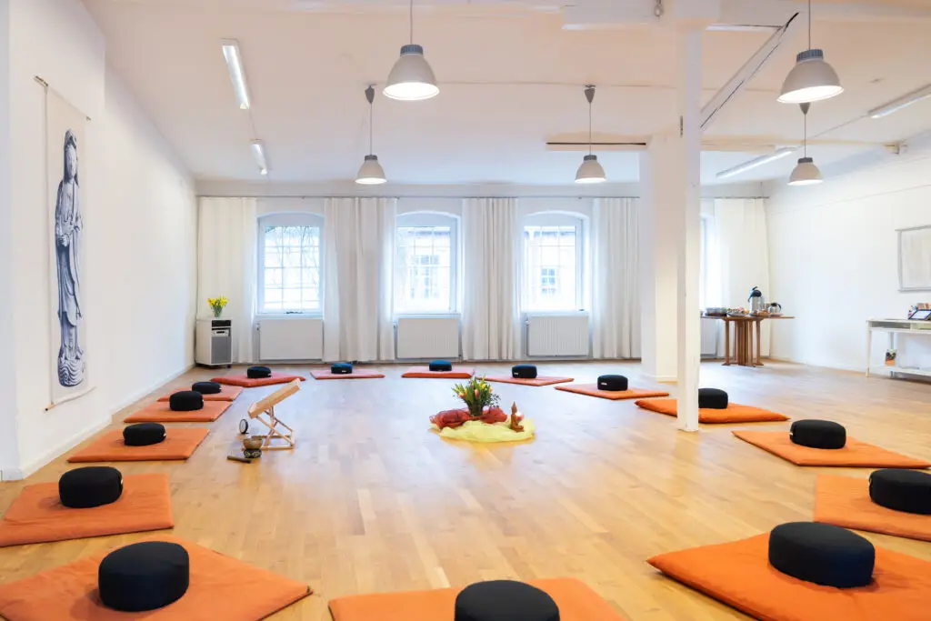 Heller Meditationsraum mit kreisförmig angeordneten Sitzkissen.