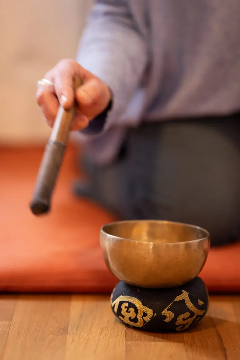 Klangschale mit Schlägel vor Meditationskissen.
