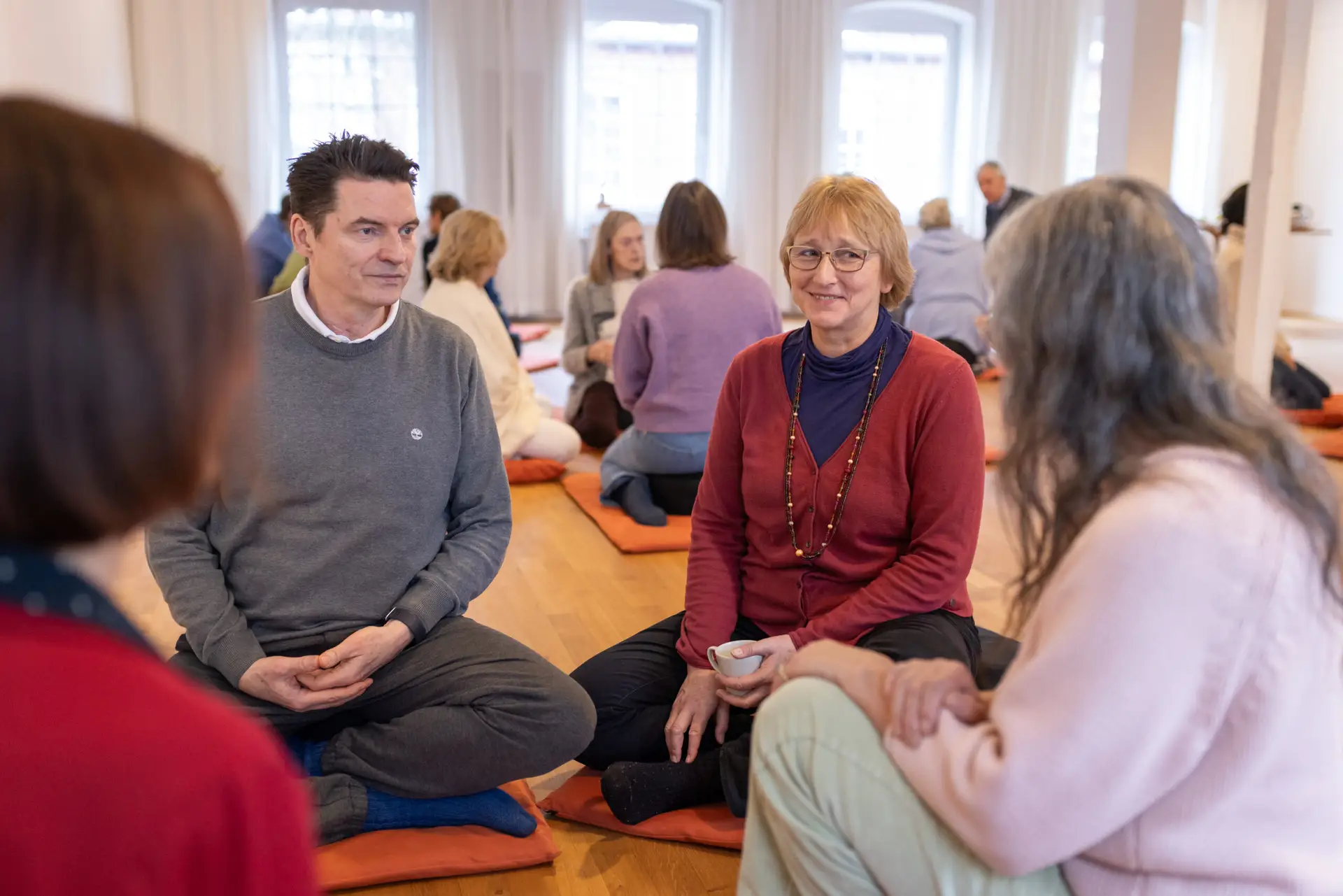Menschen im Gespräch auf Meditationskissen.
