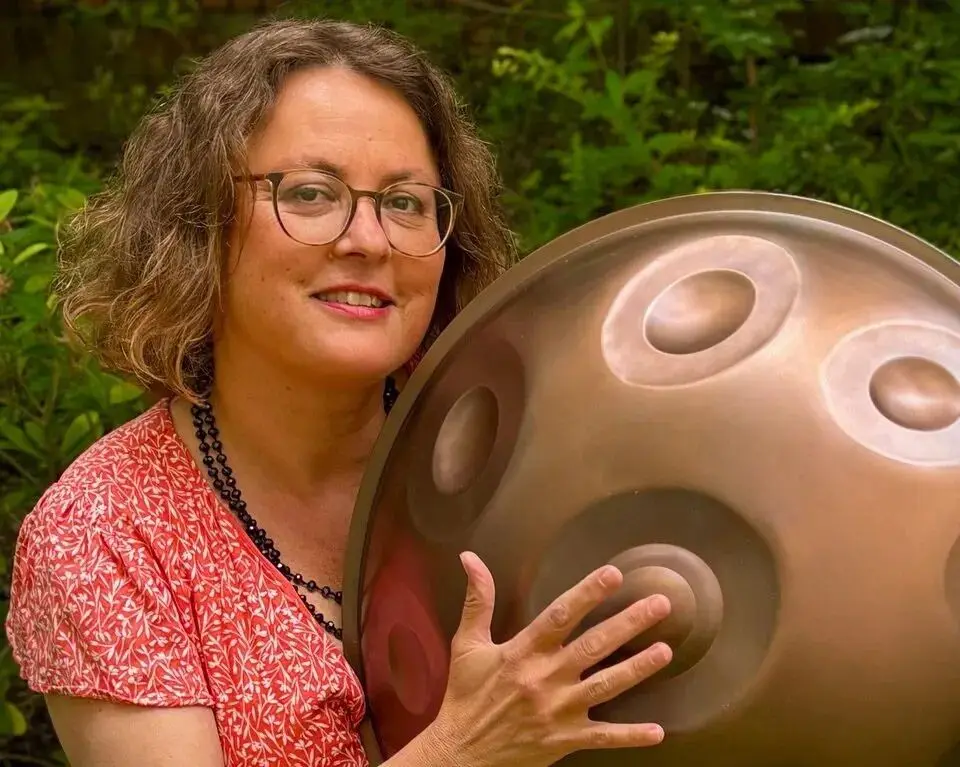 Frau mit Handpan in grüner Natur.