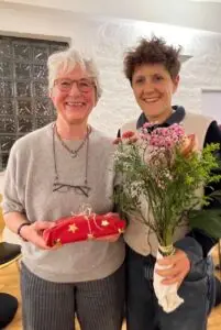 Zwei lächelnde Frauen mit Blumen und Geschenk.