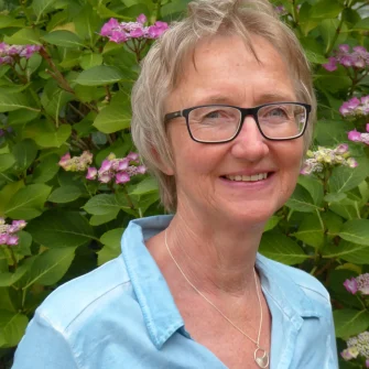 Lächelnde Frau mit Brille vor Blumen.